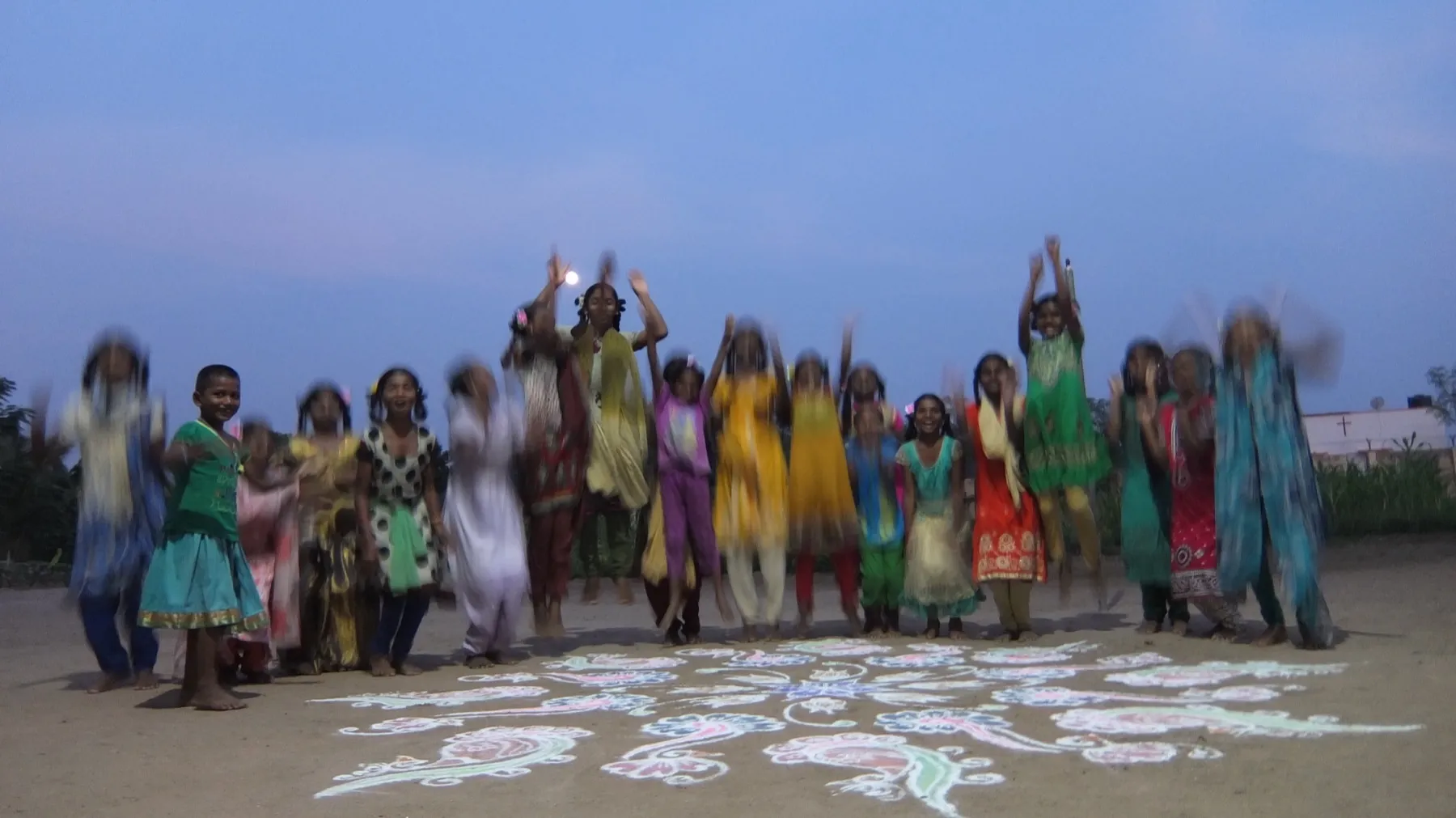 Al tramonto, le ragazze alzano le braccia attorno a un kolam disegnato a terra