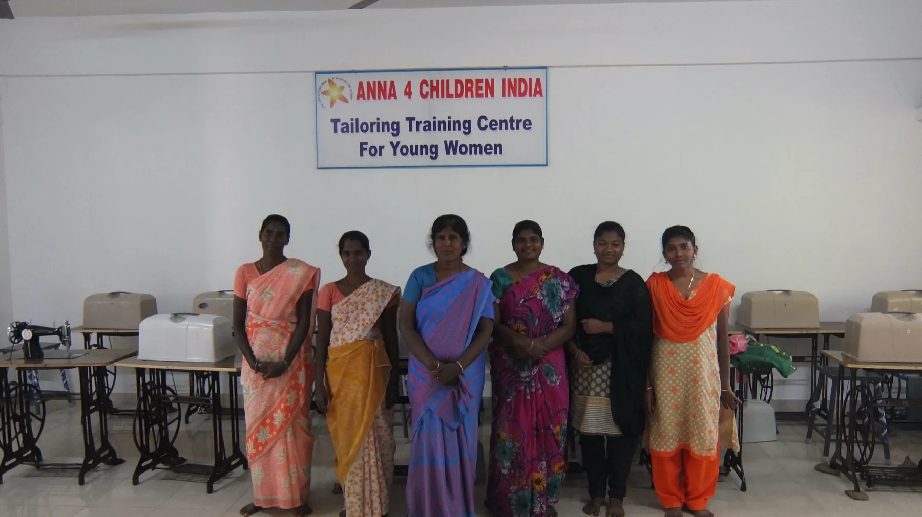 Le allieve del centro di formazione sartoriale davanti alle macchine da cucire, sotto l'insegna Anna 4 Children India Tailoring Training Centre For Young Women