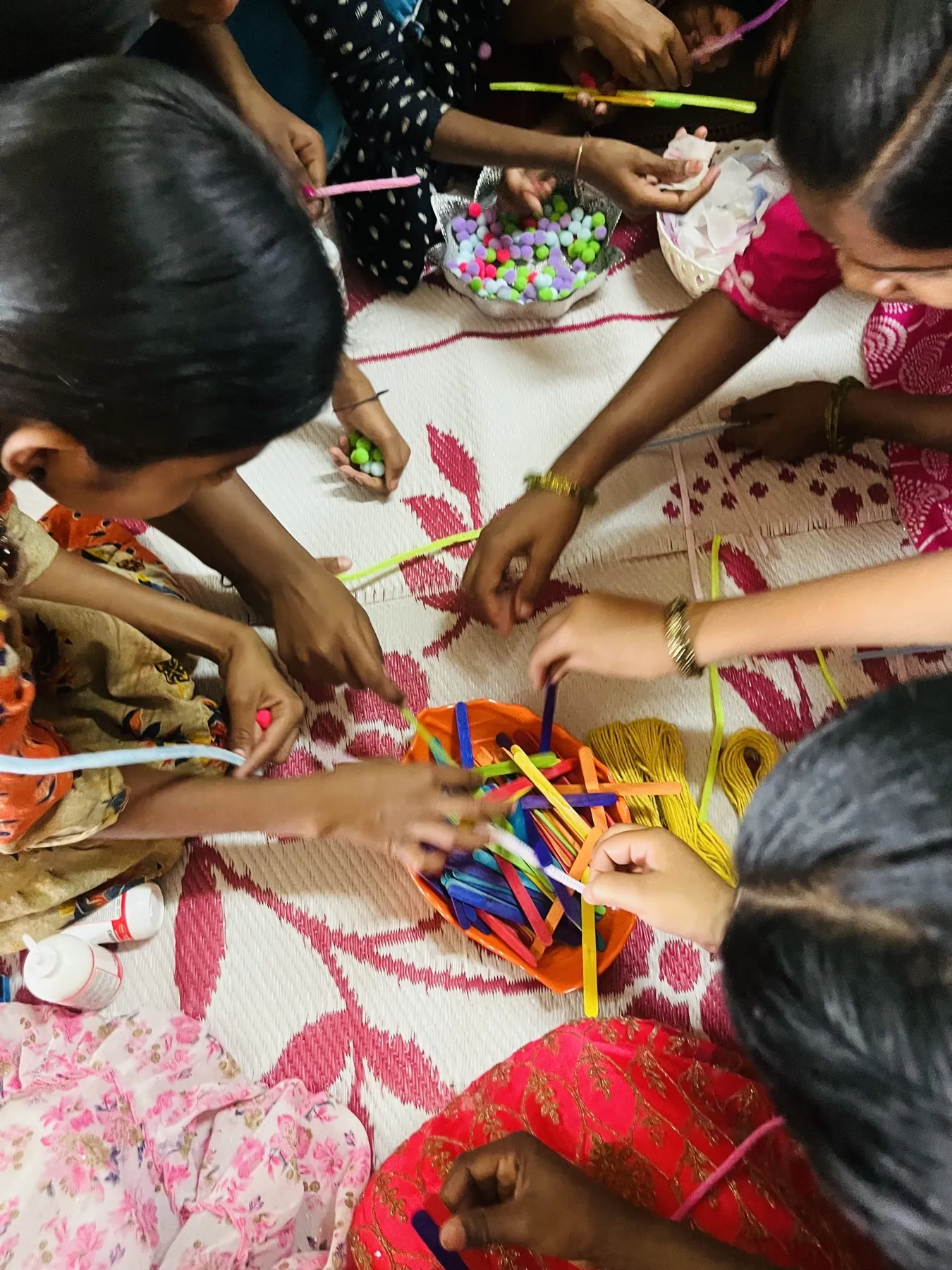 Mani di bambine che intrecciano cannucce colorate durante un laboratorio manuale